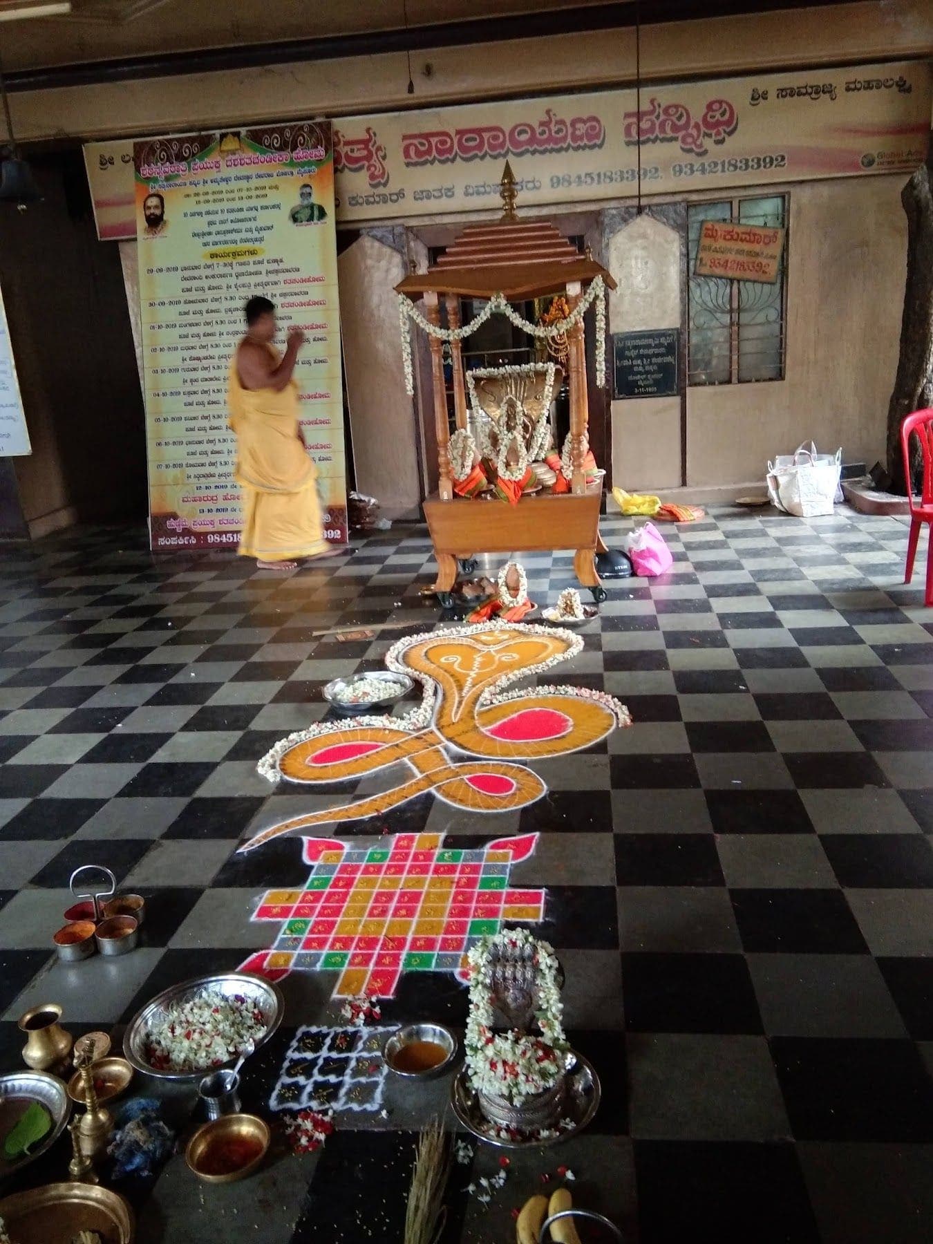 ಕಪ್ಪು-ಬಿಳುಪು ಹಾಸುಗಲ್ಲಿನ ನೆಲದ ಮೇಲೆ ಬಣ್ಣದ ನಾಗ ರಂಗೋಲಿ, ಪುಟ್ಟ ಮರದ ಚಪ್ಪರ, ಪೂಜಾ ಪಾತ್ರೆಗಳು ಮತ್ತು ಅರ್ಚಕರು