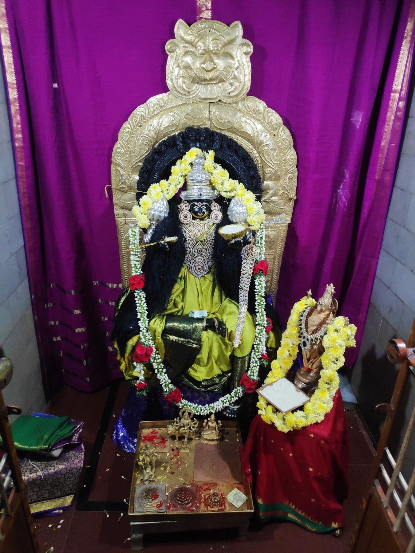 ನೇರಳೆ ಪರದೆಯ ಮುಂದೆ ಹಳದಿ-ಹಸಿರು ರೇಷ್ಮೆ ಉಟ್ಟ ಕಪ್ಪುಶಿಲೆಯ ದೇವಿಯ ಮೂರ್ತಿ ಮತ್ತು ಪಕ್ಕದಲ್ಲಿ ಪುಟ್ಟ ಅಲಂಕೃತ ಮೂರ್ತಿ; ಮುಂದೆ ಪೂಜಾ ತಟ್ಟೆ